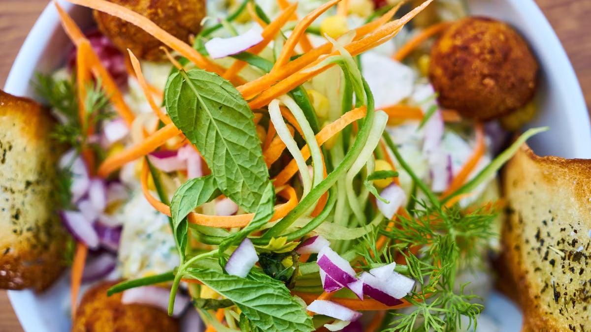 Vibrant salad featuring fresh vegetables, falafel, and herbs in a white bowl, perfect for a healthy meal.